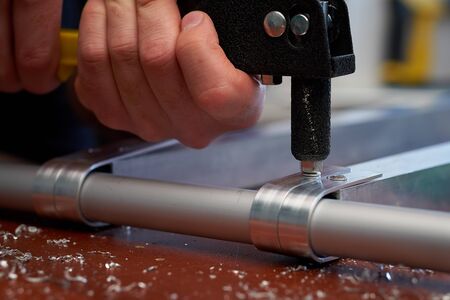 Close-up male hand holds a riveter and rivets aluminum profiles