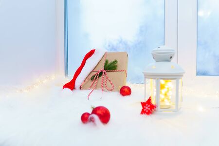 Gift box with Christmas decorations on a white windowsill near a blue window.の写真素材