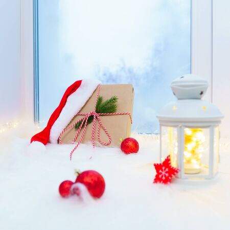 Gift box with Christmas decorations on a white windowsill near a blue window.の写真素材