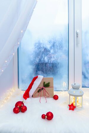 Gift box with Christmas decorations on a white windowsill near a blue window.の写真素材