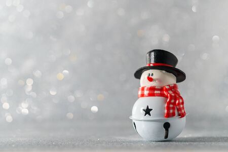A toy snowman in a black hat stands against a background with beautiful bokeh with empty space on the left.の写真素材