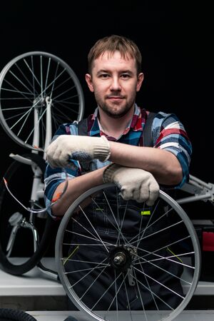A smiling craftsman holds a bicycle wheel while looking at the camera. Portrait of a bicycle service worker.の写真素材