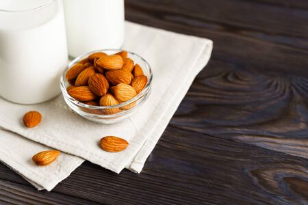 Close-up of almond milk in a glass mug and a refillable glass bottle, next to it lie almonds and a textile napkin on a wooden table.の写真素材