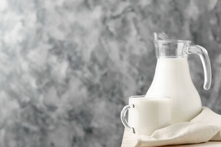 Glass jug and mug with milk on the edge of a white wooden on a concrete background.の写真素材
