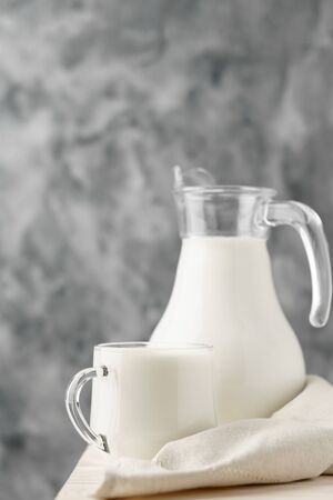 Glass jug and mug with milk on the edge of a white wooden on a concrete background.の写真素材