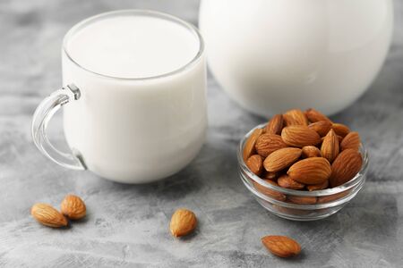 Almond milk in a glass jug and mug, next to nuts in a bowl on a concrete background.の写真素材