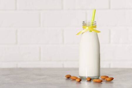 Glass bottle with almond milk, decorated with a yellow ribbon and a cocktail tube among almonds on a white wooden table. Illuminated by morning sunlight through a window.の写真素材