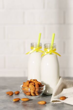 Two glass bottles with almond milk, decorated with a yellow ribbon on a white wooden table. Illuminated by morning sunlight through a window. Two cocktail rolls and a bowl of almonds in the kitchen.の写真素材