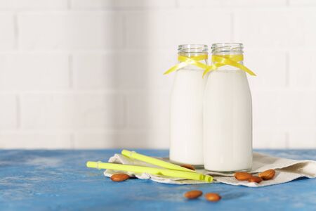 Two glass bottles with almond milk, decorated with a yellow ribbon on a blue concrete table. Illuminated by morning sunlight through a window.の写真素材
