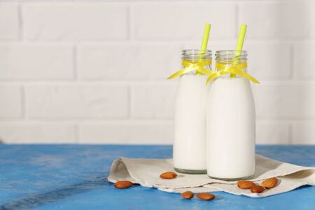 Two glass bottles with almond milk, decorated with a yellow ribbon on a blue concrete table. Illuminated by morning sunlight through a window.の写真素材