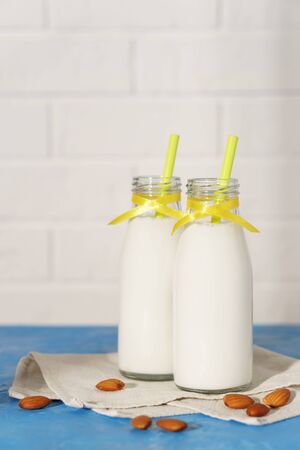 Two glass bottles with almond milk, decorated with a yellow ribbon on a blue concrete table. Illuminated by morning sunlight through a window.の写真素材