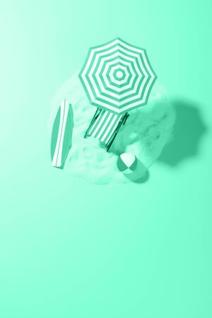 Tropical vacation background. Sun lounger with umbrella and beach accessories for active rest on the sandy island, copy space, top view. Tinted in trendy Aqua Menthe color.の写真素材