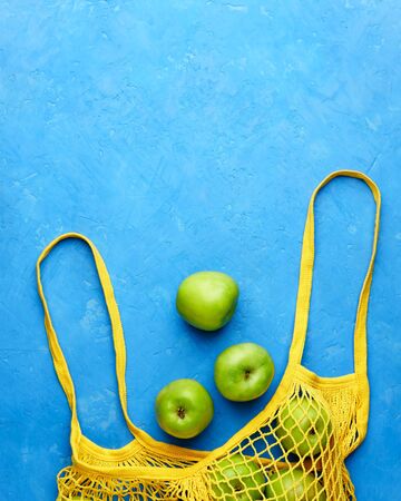 A yellow string bag with green apples lies on blue concrete. Image contains copy space, vertical.の写真素材