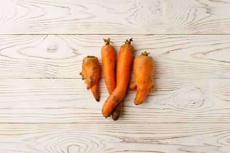 A few ugly carrots in the center of a light wooden table. The image contains a copy space, top view.の写真素材
