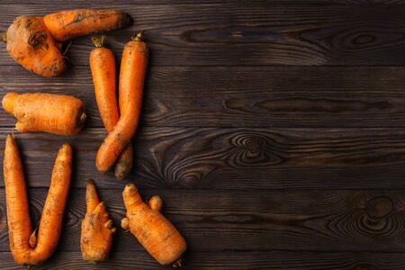 Top view at ugly carrots on a dark wooden table. The image contains copy space, horizontal orientationの写真素材