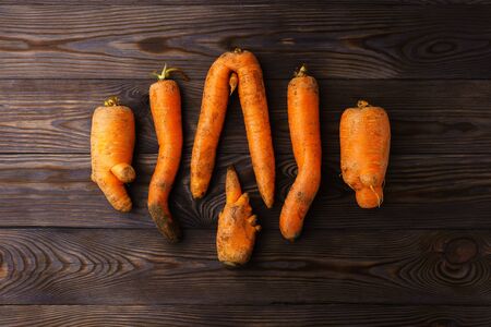 A few ugly carrots in the center of a dark wooden table. Horizontal orientation, top view.の写真素材