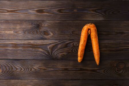 Top view at ugly carrot on a dark wooden table. The image contains copy space, top view.