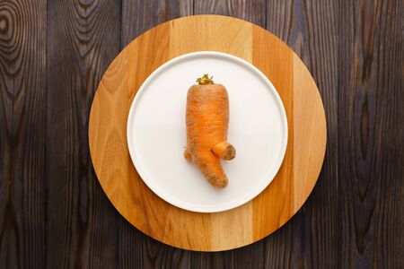 Top view of an ugly carrot on a flat plate on a dark wooden surface. Horizontal orientation.の写真素材