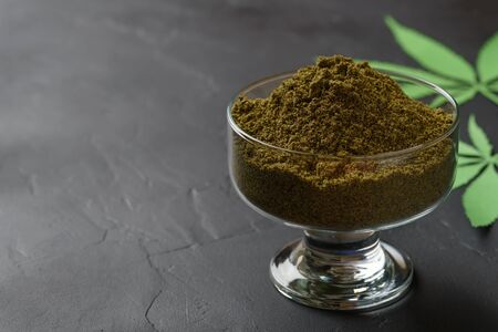 Hemp flour in a glass bowl and leaves on a dark concrete table. Horizontal orientation with copy space.の写真素材