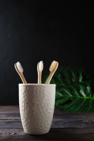 White ceramic glass with three biodegradable bamboo toothbrushes stands on a wooden table, dark background. Image with copy space. Zero waste concept.の写真素材