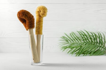 Two scrapers made of coconut bristles and a bamboo handle in a glass cup. Biodegradable kitchen accessories for washing dishes and zero waste concept. Image contains copy space.の写真素材