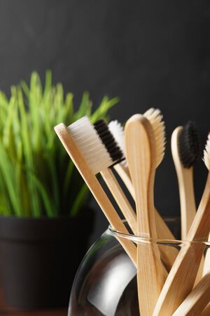 Close up of several biodegradable bamboo toothbrushes in a glass cup on a dark background. Image with copy space, vertical orientation. Zero waste concept.の写真素材
