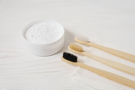 Three bamboo toothbrushes with a white textile towel and powder for brushing teeth in a bowl on a light wooden background. Horizontal orientation.の写真素材