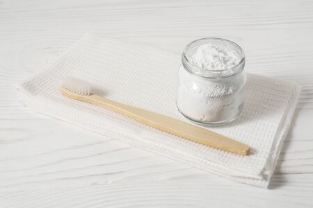 Bamboo toothbrush with a white textile towel and powder for cleaning teeth in a bowl on a light wooden background. Horizontal orientation.の写真素材