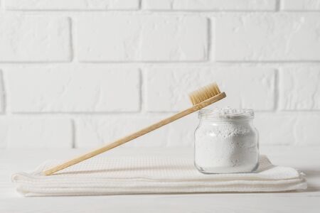 Bamboo toothbrush with a white towel and powder for cleaning teeth in a bowl on a background of a light brick wall. Horizontal orientation, image with copy space.の写真素材