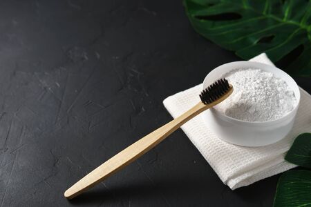 Bamboo toothbrush, tooth powder and white cotton towel on a black concrete background. Zero waste concept. Eco friendly biodegradable personal care products. Copy space.の写真素材