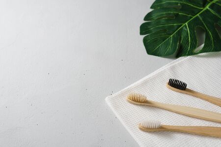 Three bamboo toothbrushes with white towel and green leaves on a gray concrete table. Zero waste concept. Eco friendly personal care products. No plastik.の写真素材