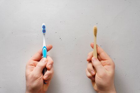 Male hands hold toothbrushes on a light gray concrete background, top view. Choose between plastic...