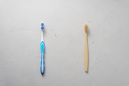 Two toothbrushes on a light gray concrete background. Top view, copy space. Choose between plastic and bamboo toothbrush. No plastic concept.の写真素材