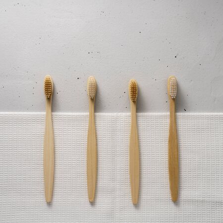 Four bamboo toothbrushes with a white cotton towel on a light gray concrete background. Top view...