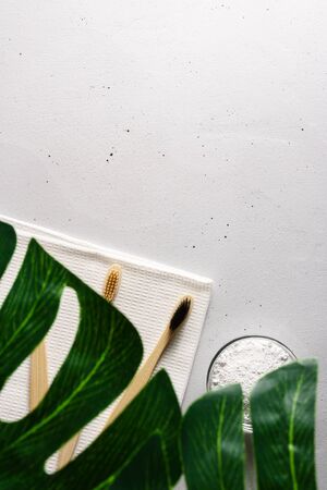 Three bamboo toothbrushes, tooth powder and towel on a light gray concrete background. Concept no plastic and zero waste. Top view, copy space, vertical orientation.の写真素材
