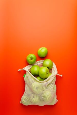 Green apples in a mesh grocery bag on a red background. Flat lay, copy space. Zero waste and no plastic concept.の写真素材