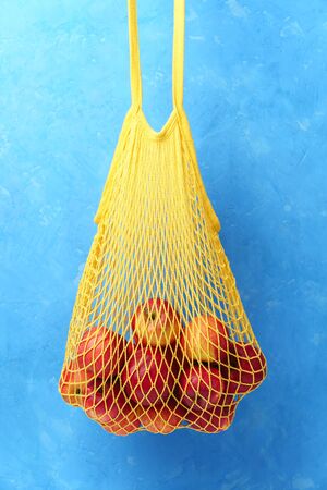 Red apples in a yellow string bag on a background of blue concrete wall. Vertical orientation.の写真素材