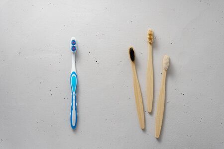Three bamboo and one plastic toothbrushes on a light gray concrete background. The choice between plastic and biodegradable products. Concept no plastic and zero waste.の写真素材