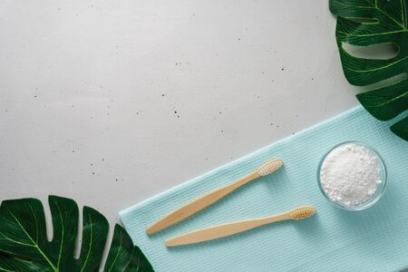 Two bamboo toothbrushes, tooth powder and a towel on a light gray concrete background. Concept no...