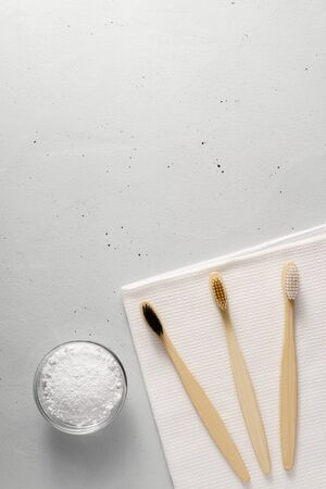 Three bamboo toothbrushes, tooth powder and towel on a light gray concrete background. Concept no plastic and zero waste. Top view, copy space, vertical orientation.の写真素材