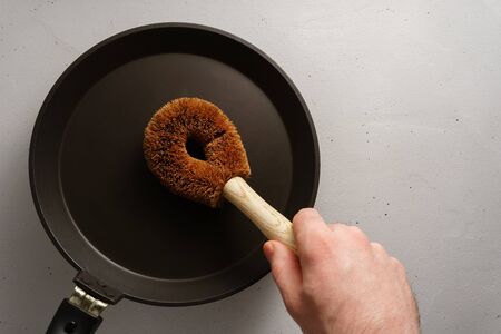 The male hand holds a brush made of coconut with a bamboo handle over the pan. Biodegradable kitchen accessories. No plastic concept.の写真素材
