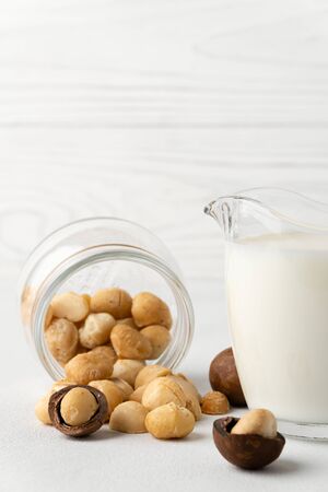 Dairy products without lactose. Scattered macadamia nuts on a white surface and macadamia milk in a glass cup. Vertical orientation with copy space. Dairy-free milk.の写真素材