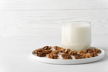 Walnut milk in a glass cup and nuts on a flat plate, white background. Dairy products without lactose. Horizontal orientation with copy space.の写真素材