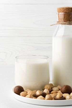 Dairy-free milk. Macadamia nut milk in a glass cup and a bottle on a flat plate, light background. Dairy products without lactose and gluten.の写真素材