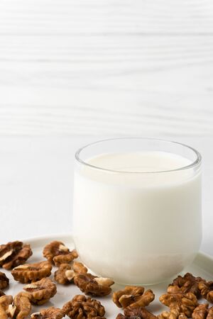 Walnut milk in a glass cup and nuts on a flat plate, white background. Dairy products without lactose. Copy space.の写真素材