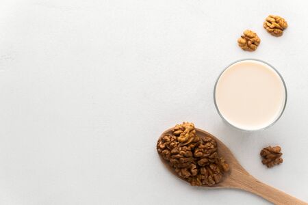 Walnut milk in a glass and a wooden spoon with nuts on a light gray concrete background. Top view, copy space. No lactose and dairy-free milk concept, vegan food.の写真素材