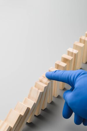Stop COVID-19. A hand in a blue medical glove stops the domino effect. Preventive measures to combat the global spread of the coronovirus pandemic. Vertical orientation, copy space.の写真素材