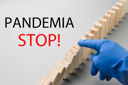 Stop COVID-19. A hand in a blue medical glove stops the domino effect. Preventive measures to combat the global spread of the coronovirus pandemic. Horizontal orientation.の写真素材
