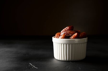 Fruit dates in a white bowl on a dark background. Copy space, horizontal orientation.の写真素材