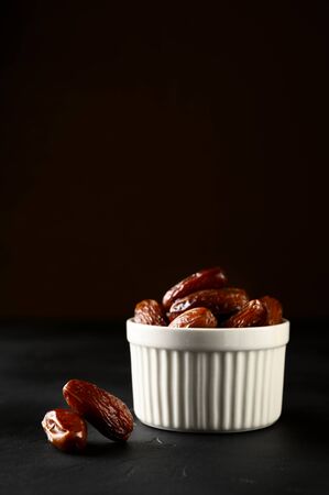Fruit dates in a white bowl on a dark background. Copy space, vertical orientation.の写真素材